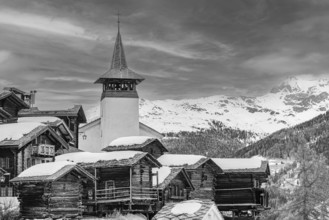 Old wooden houses with snow-covered roofs and the Saint Theodule church in the historic village