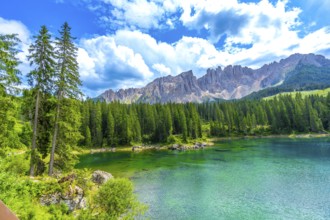 Emerald waters of lake carezza reflecting latemar mountain range, surrounded by lush pine forest