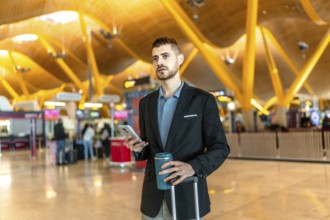 Businessman holding a reusable coffee cup and smartphone while waiting for his flight at the
