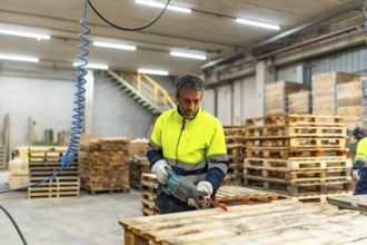 Adult caucasian man worker repairing broken pallets in a recycling plant workshop using compressed