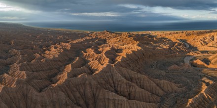 Riverbed runs through a landscape of eroded hills, badlands at sunset, Issyk Kul Lake in the