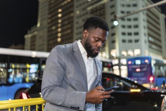 Young businessman using smartphone on a city street at night, with blurred traffic and buildings in