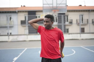 African boy stretching using rubber elastic band alone before playing basketball outdoors