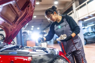 Young female mechanic wearing overalls and protective glasses is checking the oil level of a car
