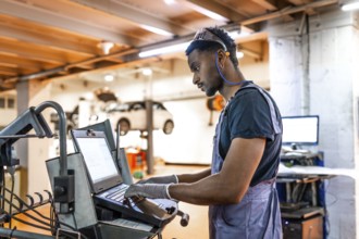 Young mechanic working diligently on a laptop for car diagnostics in a modern, well organized auto