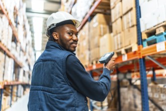 Happy african worker turning to smile while scanning packages in a large warehouse