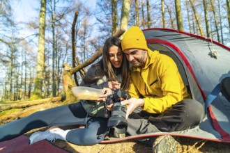 Couple of hikers reviewing photos on their camera while having a meal in front of their tent during