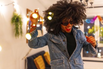 Excited latin young man with curly hair dancing playing with decoration lights at home party