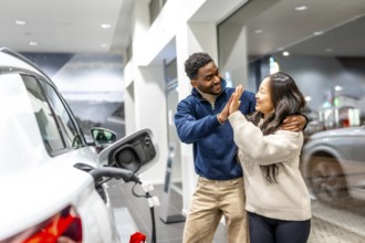 Happy multiethnic couple celebrating their new electric car purchase with a high five at the