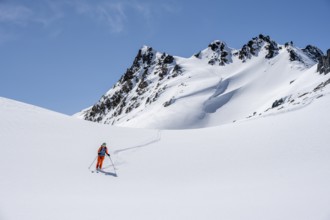 Ski tourer on the descent, minimalist winter landscape, white snow and dark mountains on the