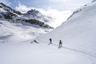 Atmospheric clouds in a wintry mountain landscape, ski tourers on the ascent to Porta d'Es-cha,