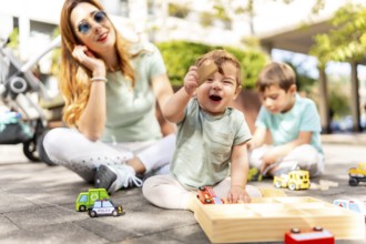 Baby holding a toy and laughing next to his family playing together on an urban park