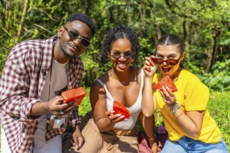 Three joyful friends enjoying fresh watermelon slices while relaxing at a sunny summer picnic in a