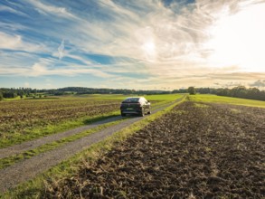 A car drives on a rural road between ploughed fields under a partly cloudy sky, Carsharing, VW ID5,