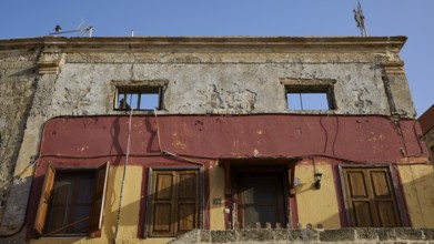 Old building with damaged walls, two windows and doors painted in yellow and red, Rhodes Old Town,