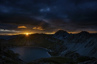 Lake Lüner See with Montafon mountains and dramatic cloudy sky at sunrise, Tschagguns, Rätikon,