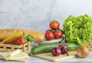 Colourful peppers, tomatoes, cucumber, lettuce and slices of cheese next to a baguette on a table,