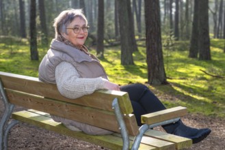 Elderly woman, 65 years old, sitting on a bench and enjoying nature in the forest in Ystad, Skåne,