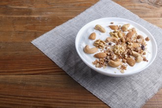 White plate with greek yogurt, granola, almond, cashew, walnuts on brown wooden background. close