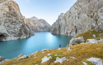 Young man at the turquoise mountain lake Kol Suu with rocky steep mountains, Kol Suu Lake, Sary
