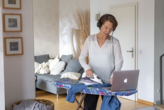 Woman, mid-50s, works from home, with laptop and communicates with colleagues via headset, home