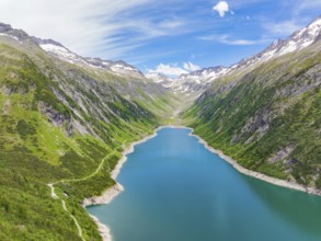 Blue lake, surrounded by high mountains and green, overgrown terrain under a bright blue sky, Klein