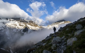 Silhouette of a mountaineer in front of a cloudy, atmospheric mountain landscape, rocky
