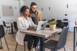 Two businesswomen collaborating on a laptop in a modern office, demonstrating teamwork and