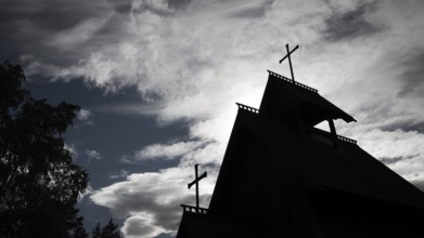Silhouette of a church with two crosses against a dramatic cloudy sky, backdrop Kristin