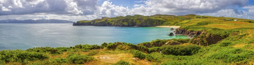 Panoramic view of a picturesque coastal landscape with cliffs, green grass and calm sea under a