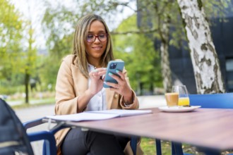 Relaxed beauty latin businesswoman using mobile sitting on an outside cafeteria
