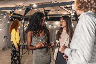 Multi-ethnic young people in elegant clothes chatting during night party at terrace