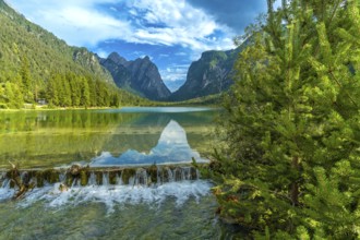 Crystal clear water cascading from a small waterfall into lake dobbiaco, reflecting the majestic