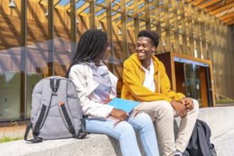 Two male and female african students talking sitting together in the university campus in a sunny