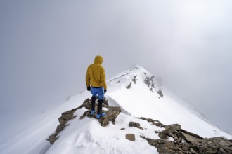 Ski tourer on the cloudy summit of Kesch Pitschen, Bündner Haute Route ski tour, Albula Alps,