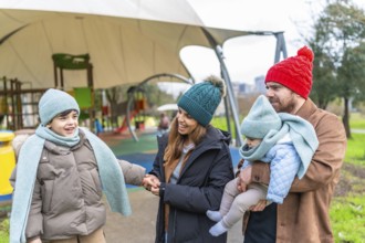 Smiling family bundled in warm winter clothes, enjoying a joyful day together at the playground,