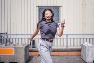 Asian woman dancing energetically k-pop style dance outside an industrial building