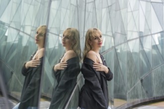 Fashionable pose of a young blonde in a glass buildings in the city, young man in a black suit