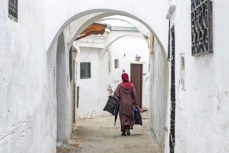 Moroccan Muslim woman in traditional Islamic dress wearing hijab walking with shopping bags in