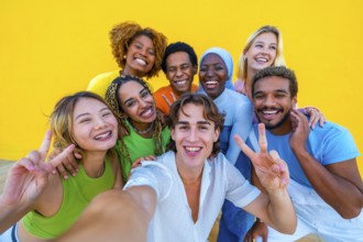 Multi-ethnic friends gesturing success while taking a selfie next to a yellow wall