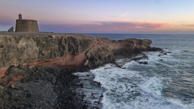 Cliffs and a defence defence tower by the sea at sunset with a colourful sky, Play Blanca,