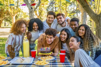 Young man smiling about to blow candles celebrating birthday with multi-ethnic friends at park