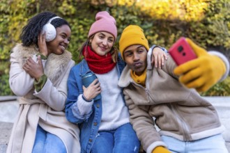 Three young friends wearing winter clothes taking a selfie with smartphone in a city park