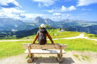 Hiker relaxing on a bench and admiring the odle mountains in val di funes, south tyrol, italy