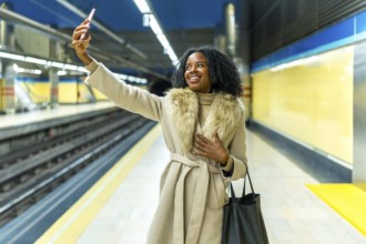 Smiling businesswoman enjoying a selfie with her smartphone while waiting for the subway train at a