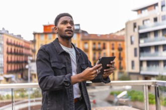Casual young african man looking up while using digital tablet in the city