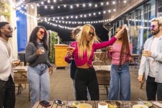 Blonde woman dancing among multi-ethnic friends at night party in a bar terrace in the city