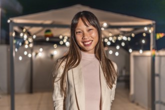 Portrait of a happy cute asian woman standing smiling at camera in a night roof party