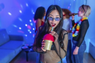 Asian woman drinking a colorful beverage at a lively party with friends, enjoying the music and