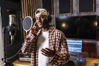 Young happy african american male singer wearing headphones and singing in professional recording